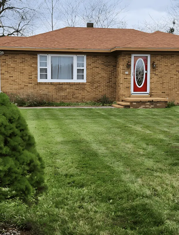 Well-manicured front lawn of a local brick home with a red door, showcasing professional lawn care results